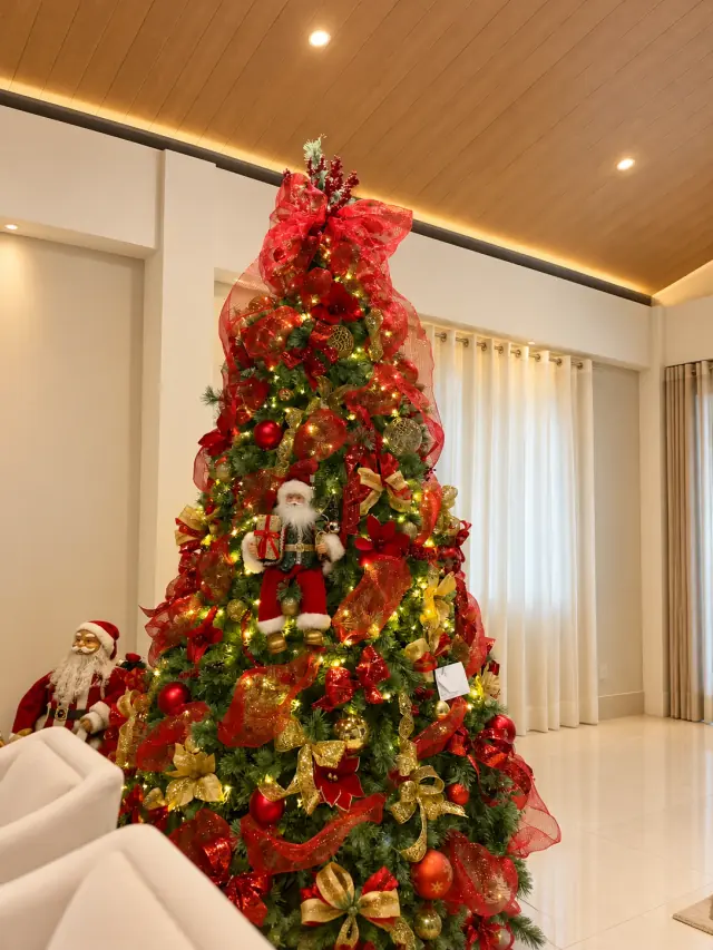Árvore de Natal clássica com laços vermelhos e dourados, flores e luzes quentes em uma sala.